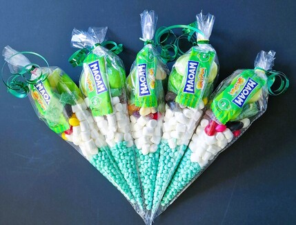 A colorful assortment of sweets and candies arranged in a transparent cone-shaped plastic bag, sealed with a green ribbon at the top.