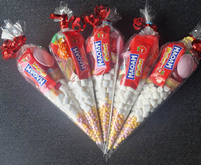 A colorful assortment of sweets and candies arranged in a transparent cone-shaped plastic bag, sealed with a red ribbon at the top.