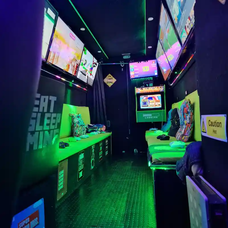 Inside the Streetside Gaming Bus set up for a Roblox party with green seating, controllers and multiple gaming screens