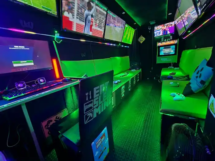 Inside the Streetside gaming bus with multiple screens, consoles, green seating and neon lighting.