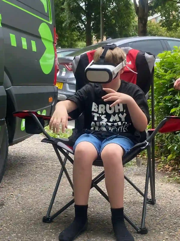 Child using an outdoor VR headset beside the Streetside Gaming Bus in Great Dunmow