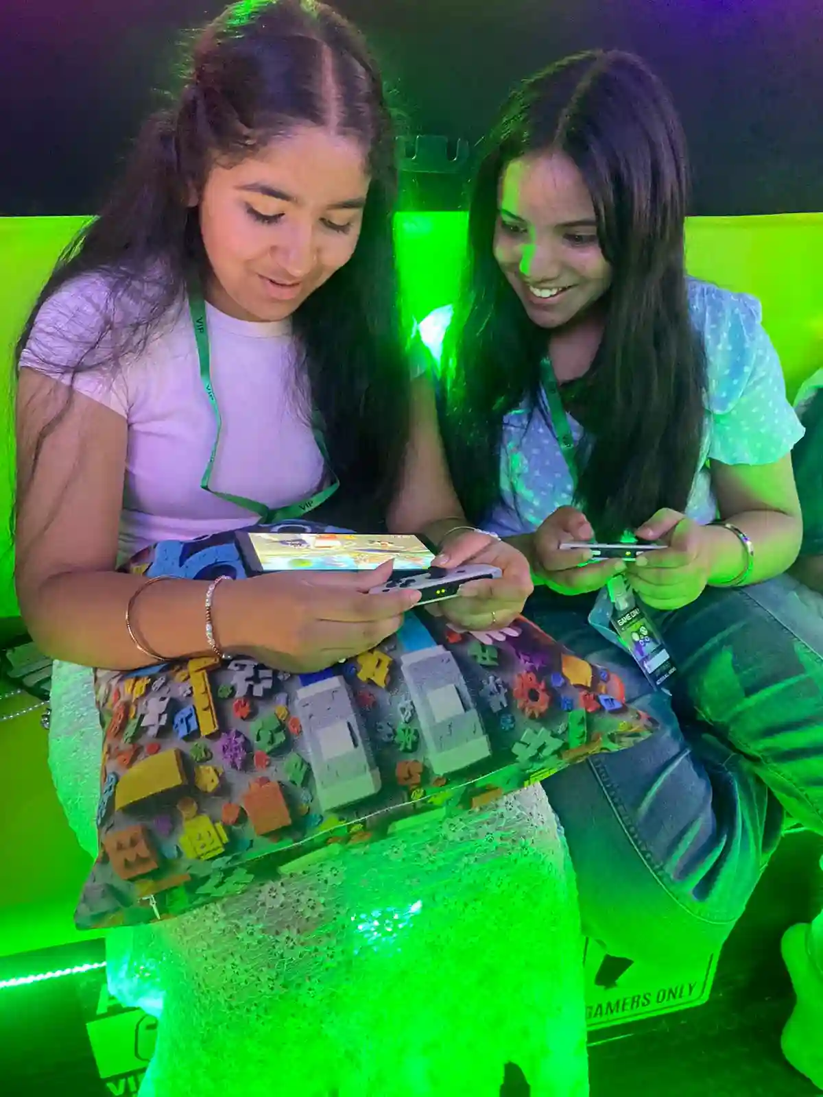 Two guests playing video games with controllers inside a neon green-lit gaming bus.
